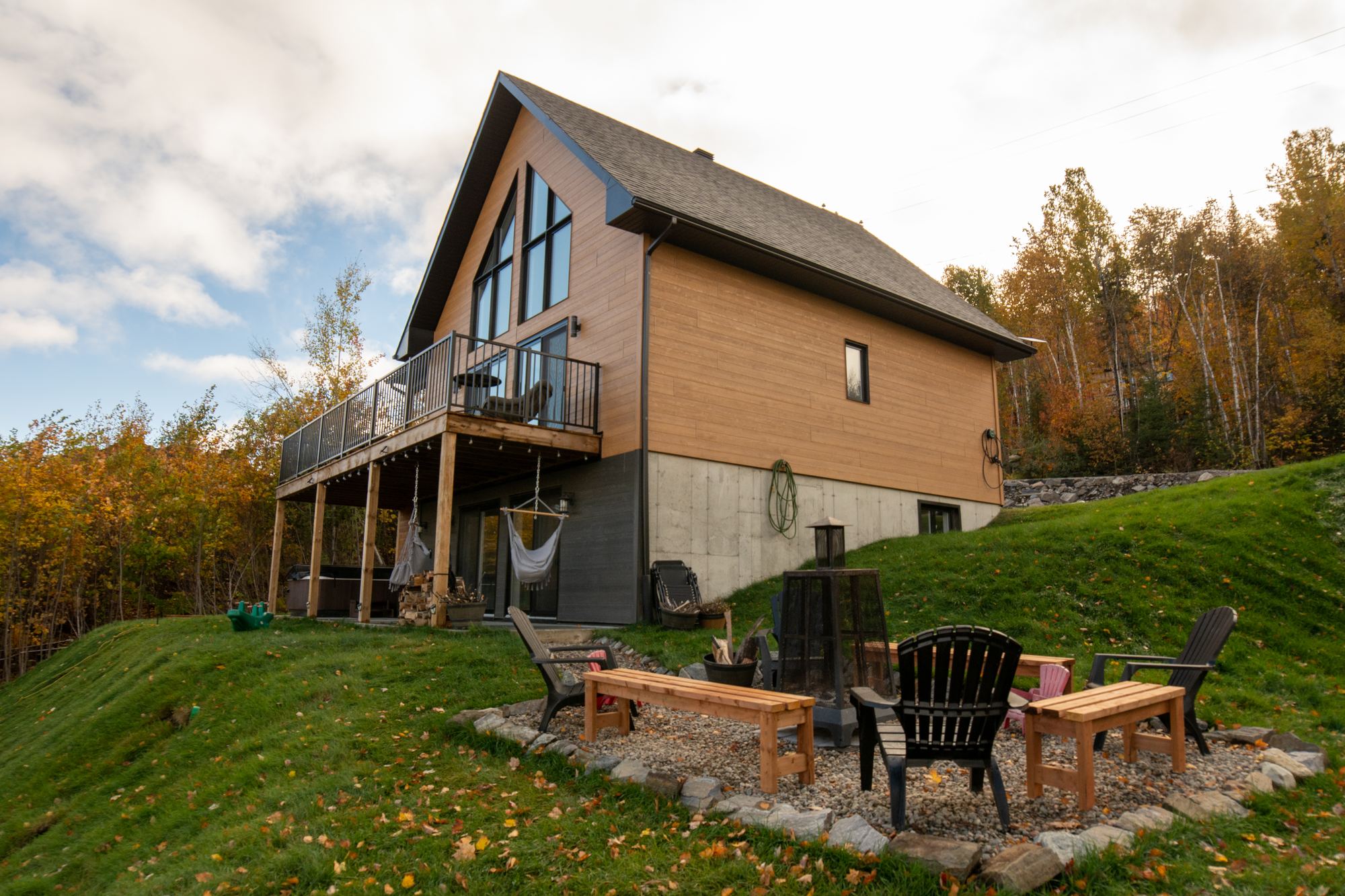 Le Chalet Ludik vu de l'arrière, avec son grand balcon, le foyer extérieur et les arbres en couleurs d'automne